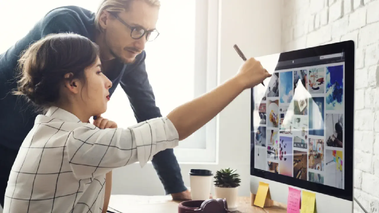 A woman seated in front of a computer screen, showing images to her co-worker, representing the collaborative process of designing a websites for their business